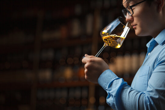 Sommelier Pouring Sample of Wine Into Glass Against Filled Bottles Shelf in Cellar 