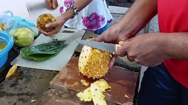 Peeling a Ripe Pineapple on a Wooden Board with Sacred Bael Fruit Aegle Marmelos visible for Traditional Sri Lankan Palathuru Wattiya Pooja