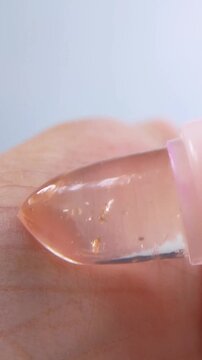 Applying transparent pink lip balm on palm. Close up view on white background. Showing skin texture and shiny reddish glossy finish. Lip care beauty concept.
