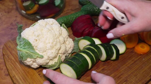 Vegetables, zucchini, cauliflower slicing on wooden board in kitchen to prepare healthy vegan salad for lunch during cooking process at home