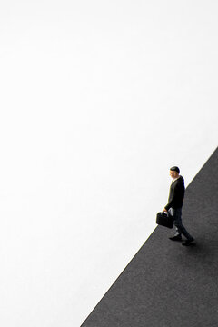 Miniature businessman carrying a briefcase walking along a diagonal dividing line between black and white backgrounds. Transition, risk, corporate choice, moral duality concept. Copy space for text