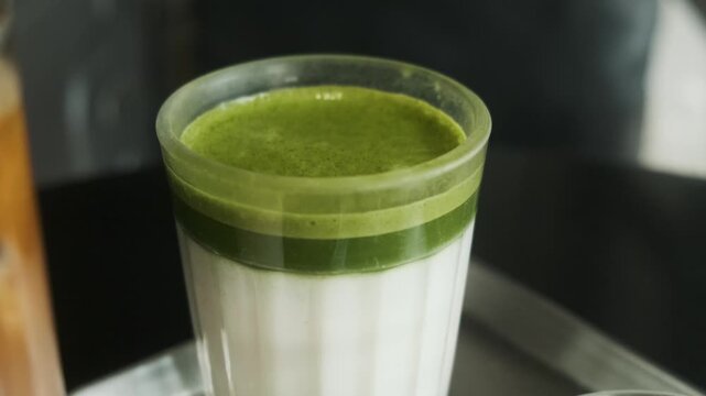 Green tea matcha latte with vibrant green layer over cold milk served in glass on metal tray in cafe. Healthy drink. Japanese tradition and contemporary aesthetics