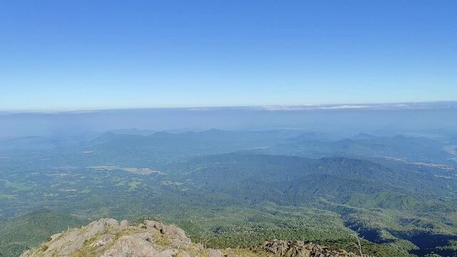 Breathtaking panoramic view from a majestic mountain peak, showcasing an endless expanse of lush green forests under a clear blue sky, extending to a distant hazy horizon