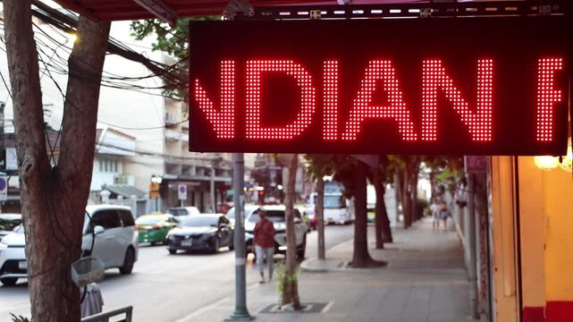 Close-up of an illuminated red LED scrolling sign advertising Indian food on a city street in Bangkok