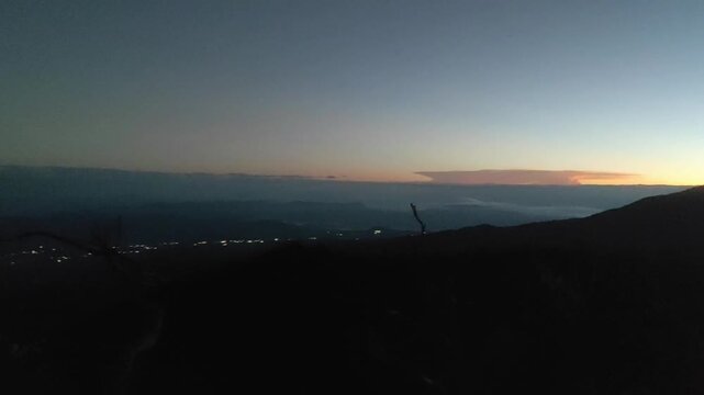 Majestic panoramic view overlooking a serene mountain range and a distant city, capturing the tranquil beauty of pre-dawn light stretching across the vast, awakening horizon