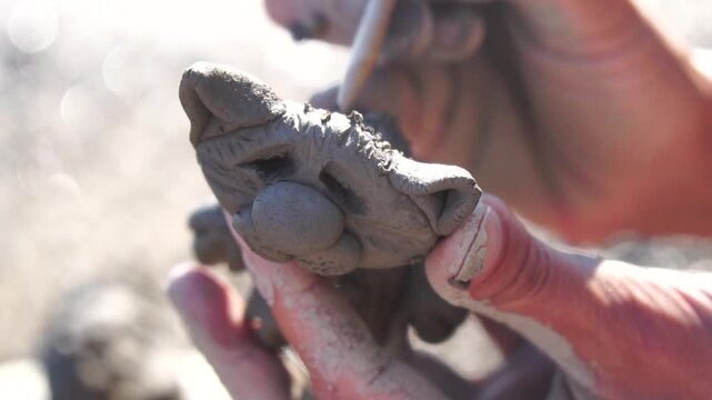 Clay sculpture hands, artist meticulously crafting a small cat figure with tools on a sunny outdoor day