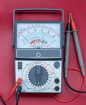 Analog Multimeter with Test Probes on Red Background - Electrical Measuring Instrument