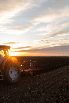 Tractor plowing plow the field on a background sunset.