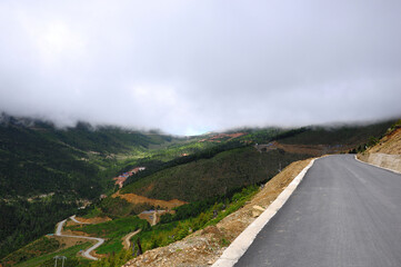 Misty mountain road winding through lush green valleys and rolling hills © Gloream