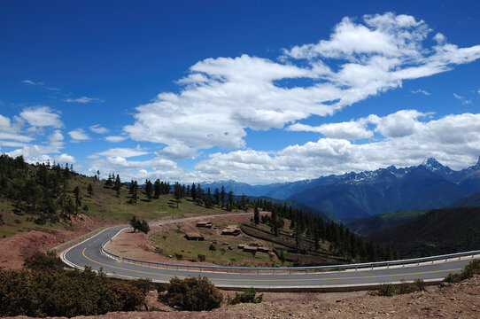 Winding mountain road under a clear blue sky with white clouds