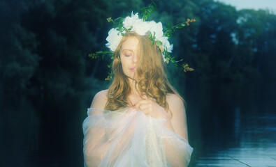 Dreamlike fine art portrait of a young woman with floral crown and translucent fabric standing in calm water at blue hour, surrounded by a mystical and peaceful natural atmosphere © ullision