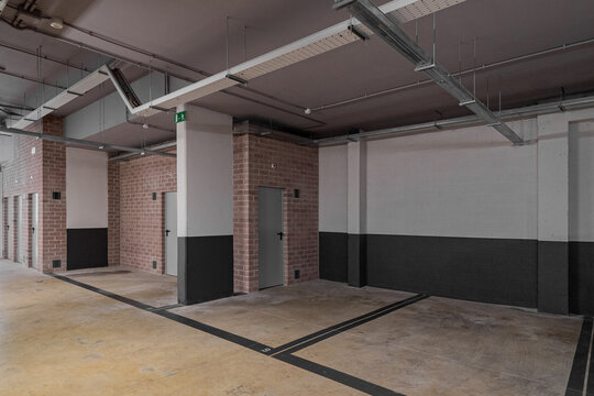 Empty modern parking garage with concrete floors and brick walls. Industrial design with minimalistic features and no vehicles present.