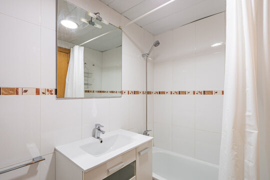Modern bathroom with a shower, white tiles, and a mirror. Features a sink and a bathtub. Clean and minimalistic design