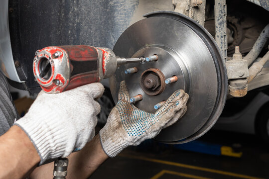 Auto mechanic in gloves using pneumatic impact wrench to tighten brake disc mounting bolt on car hub at repair service close-up