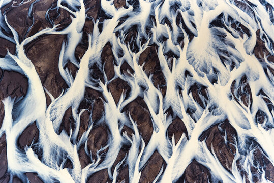 Aerial abstract view of braided glacial river channels creating intricate white patterns on dark volcanic sand, Iceland.