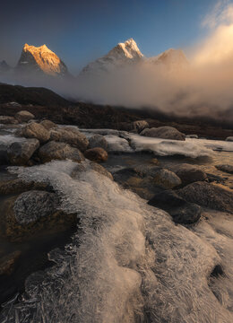 Frozen ice crystals in the foreground with snow-capped Himalayan peaks (Ama Dablam) emerging from morning mist, high altitude Everest region, Nepal.