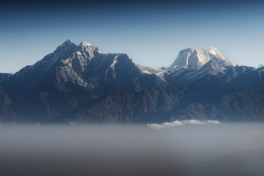 Snow-capped Himalayan peaks rise dramatically above a sea of clouds, aerial view from helicopter en route to Lukla, Nepal.