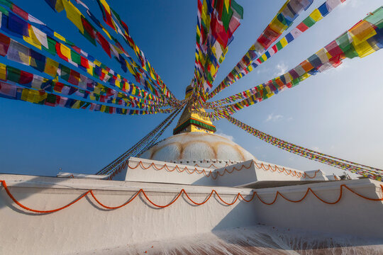 Colorful prayer flags fan out from the golden tower of Boudhanath Stupa under a clear blue sky, Kathmandu, Nepal.
