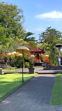 Row of yellow fringed umbrellas lining paved garden walkway toward pavilion under bright blue sky