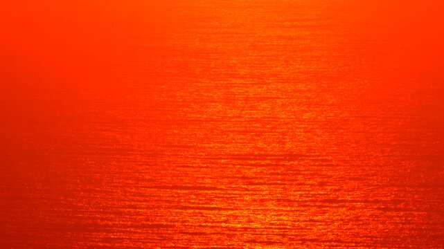 Sunset ocean water reflection creates a stunning red and orange abstract background pattern across the sea surface