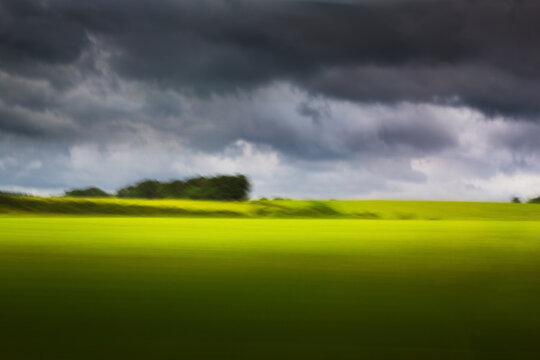 art Nature in motion from train window, abstract blur with dramatic storm sky over green field