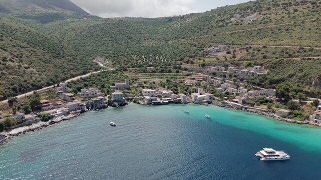 Aerial descending shot of coastal fishing village Limeni on Mani peninsula, Turquoise waterfront old stone house towers on steep lush green mountains on a sunny day, Peloponnese