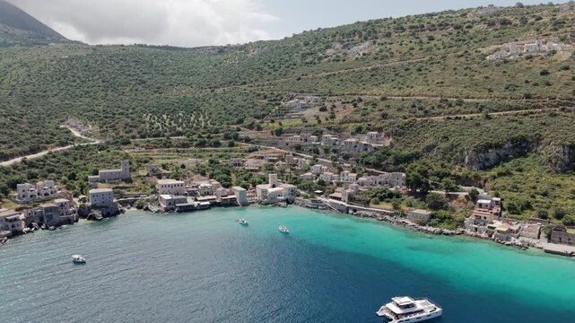 Wide aerial shot of Limeni village on Mani peninsula, Turquoise waterfront old stone house towers on steep lush green mountains with mediterranean scrub, olive grove on a sunny day, Peloponnese