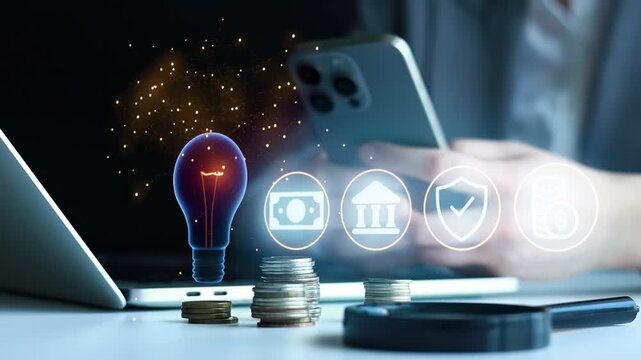 A person uses a smartphone while sitting at a table with a laptop and coins. Digital icons related to finance and security appear above the device.