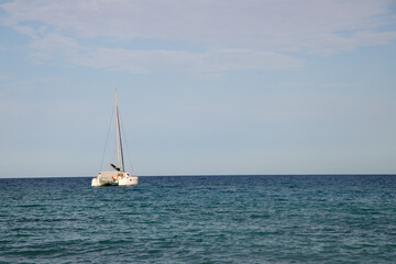 Fototapeta premium Catamaran sailing on calm blue ocean waters under a clear sky with soft clouds in the background, creating a serene maritime scene