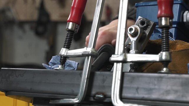 A engineer TIG welds metal structural parts, which are fixed with clamps. He wears a protective mask and gloves to avoid injury from hot sparks