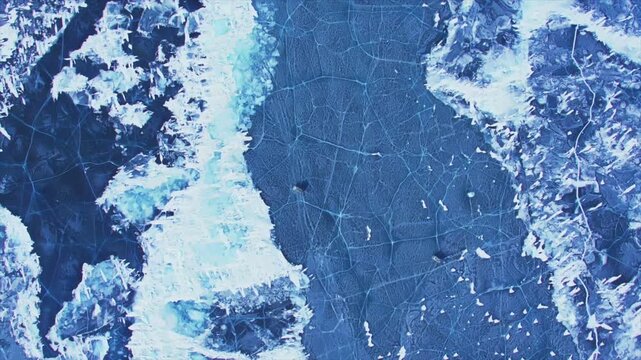 Aerial top down view of a frozen lake surface with deep blue ice, cracks, and ice floes