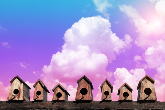 Row of small wooden birdhouses against colorful pastel sky background