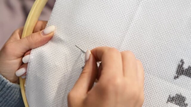 Hand crafting black thread letter y cross stitch on white fabric hoop in natural light