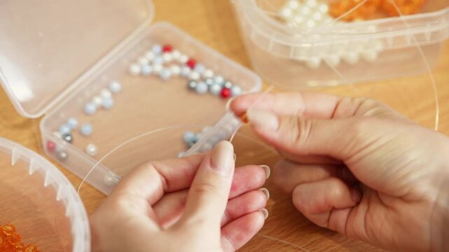 Hands threading pearl and metallic beads on string for delicate beadwork craft in warm natural light