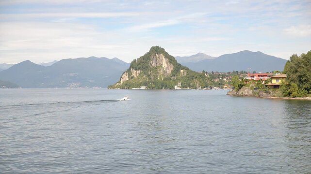 Lake Maggiore Italy summer landscape with motorboat in motion toward Calde, blue sky, mountains and rocky shoreline, scenic Italian travel destination, static tripod shot commercial video