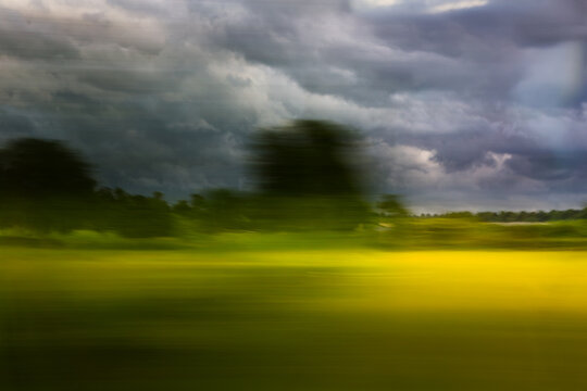 Nature in motion blur from a train window, dramatic stormy sky over a green and yellow field. Abstract travel background for  design