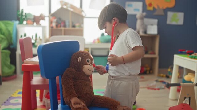 Boy holds red toy stethoscope to plush monkey and lifts earpieces to his ears while standing in a playroom building; playful curiosity.