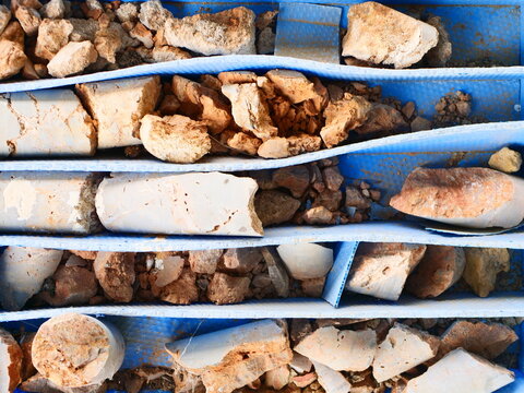 Top down view of fragmented rock and soil drill core samples inside a blue plastic container