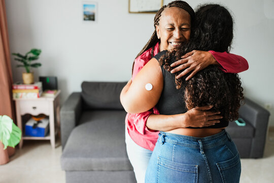 African mother hugging her daughter with diabetes patch - Family lifestyle and people diseases concept - Focus on mother hands