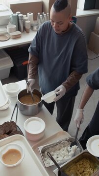 Vertical shot of diverse volunteers serving hot soup and rice into bowls at charity kitchen. Clip is ideal for humanitarian aid campaigns and corporate social responsibility videos