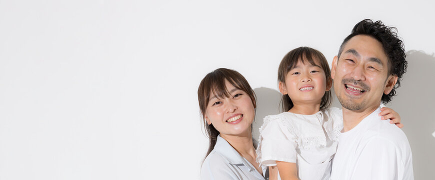 白背景で仲良し笑顔の家族・幸せなファミリーライフと健康的な暮らし　半袖夏休みイメージカメラ目線のバナー　左にコピースペースあり
