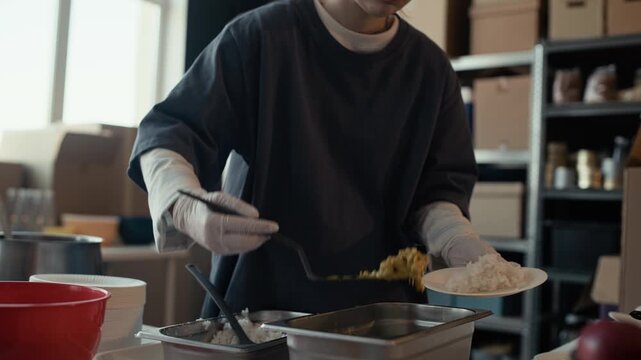 Young adult female volunteer serving hot food onto plate and handing it to Black man at community shelter. Clip is perfect for charity campaigns and corporate social responsibility videos