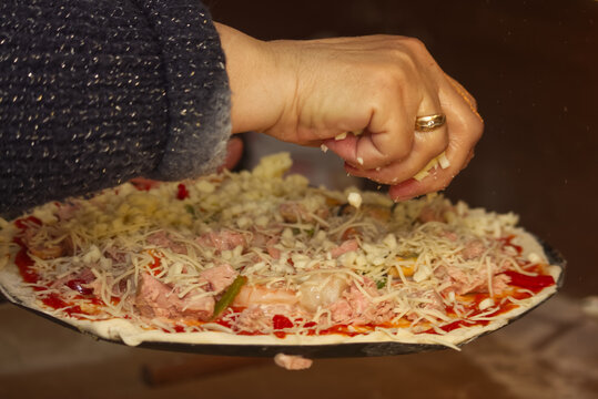 Pizza maker's hand sprinkling grated cheese over a pepper and tuna pizza