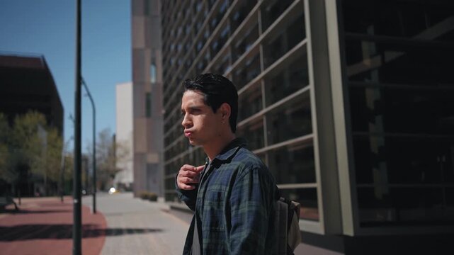 Young hispanic student walking out of modern office University building carrying backpack going home after work
