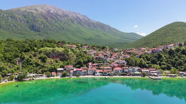 Drone approaches Trpejca Beachfront with mountain reflections on Lake Ohrid.