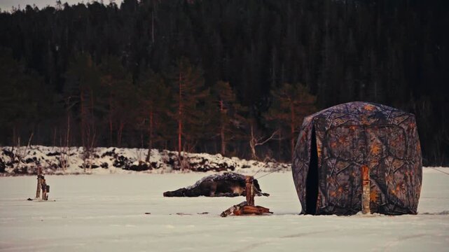An Ice Fishing Tent Stands On A Frozen Lake During Winter In A Cold Outdoor Landscape. Static Shot