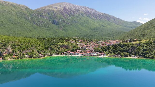 Drone approaches Trpejca Beachfront with mountain reflections on Lake Ohrid.