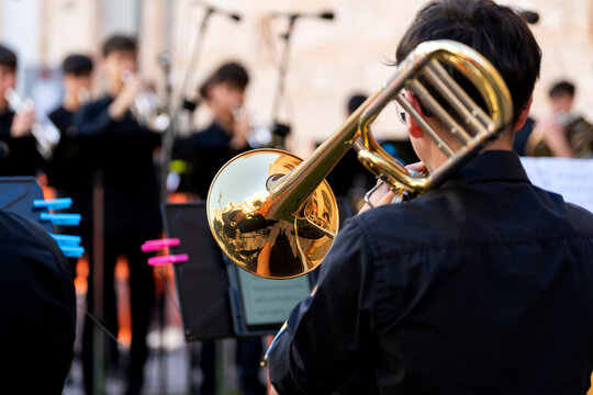 Young musician playing trombone with brass band in outdoor street concert
