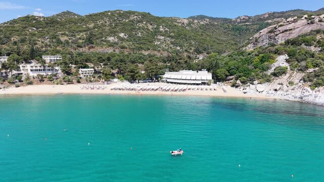 Drone circles a small fishing boat in crystal-clear water, with Kavala beaches, rocky shoreline and the beautiful coastal landscape visible all around.