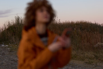 Fototapeta premium Woman lifestyle outdoors in field at sunset, blurred tall grass and path, woman in warm coat, soft bokeh light, calm nature mood, cinematic portrait